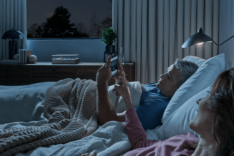 Two people lying in bed at night while looking at phone